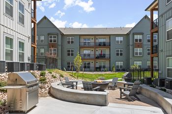 an outdoor patio with a grill and chairs in front of an apartment building at Upland Flats, Colorado, 80922